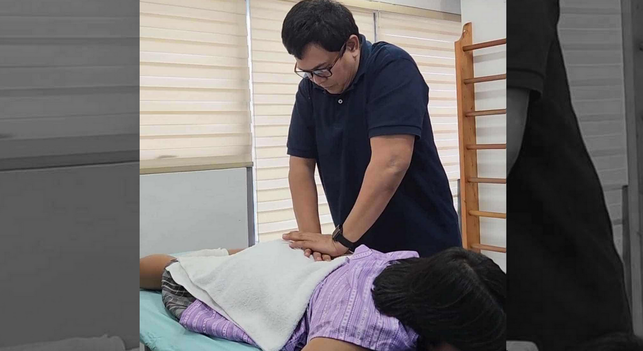 Physical therapist applying manual therapy techniques on a patient lying face down to relieve scoliosis-related back pain and improve mobility.